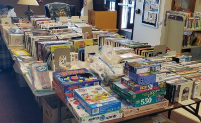 "Books, movies, and puzzles on tables at Friends of the Library book sale."
