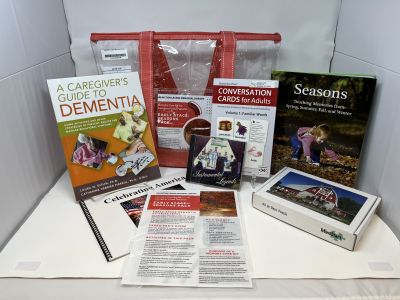 "Early Stages: Season's Pack red lined clear bag sitting behind books, cards, and CDs on white background"
